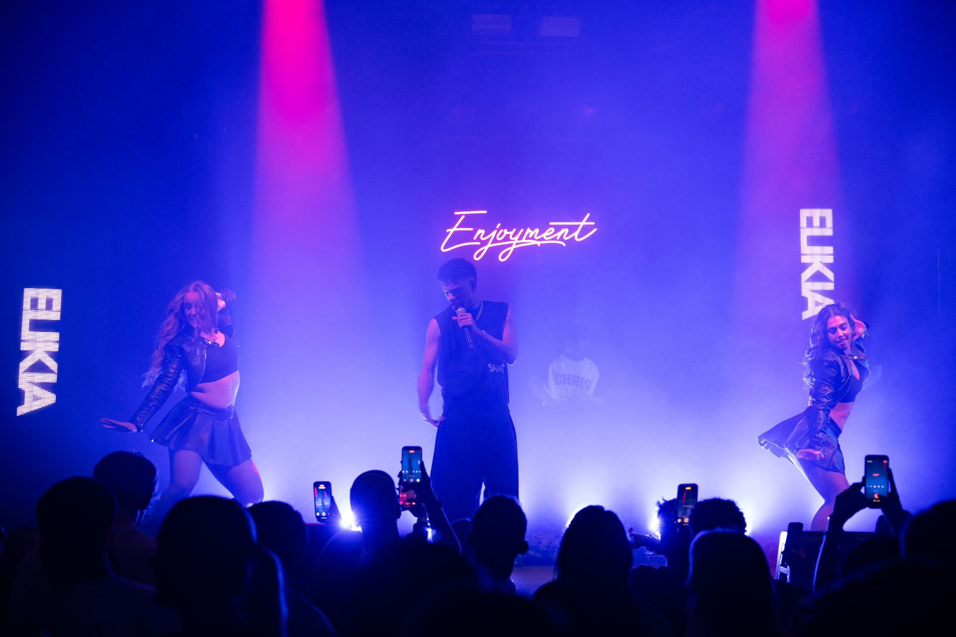 ELIKIA on stage with dancers in front of the Enjoyment neon sign